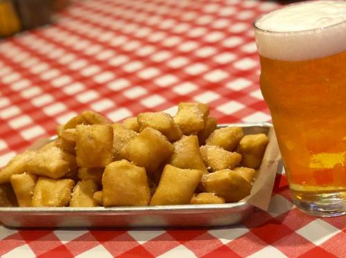 A tray of golden, sugar-dusted pastries next to a frothy glass of beer on a red and white checkered tablecloth.