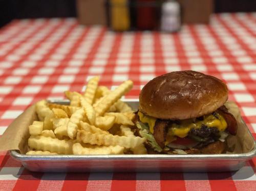 A juicy cheeseburger with bacon, lettuce, and tomato, served with crispy crinkle-cut fries on a checkered tablecloth.