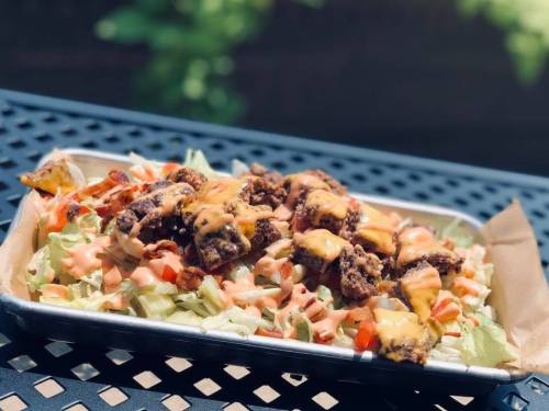 A tray of salad topped with crispy chicken, cheese, and drizzled with sauce, set on a table outdoors.