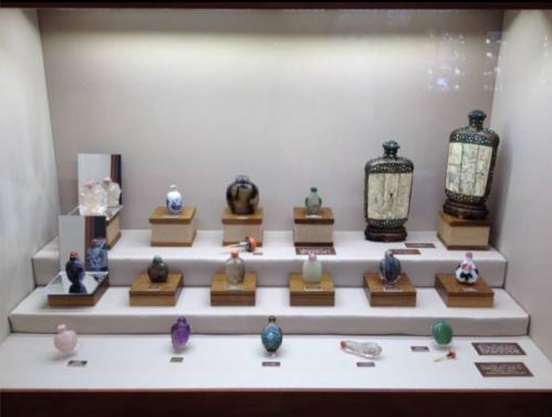 Display of decorative snuff bottles in various colors and designs, arranged on wooden stands in a glass case.