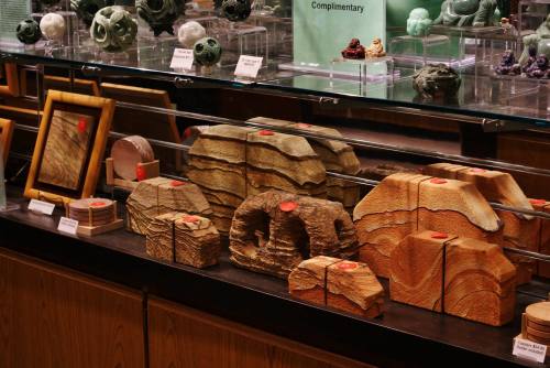 Display of various wooden sculptures and framed art pieces in a shop, with some items labeled with red tags.