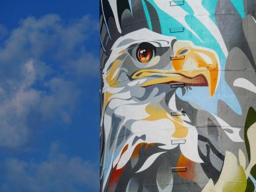A vibrant mural of an eagle's head on a concrete structure against a blue sky with clouds.