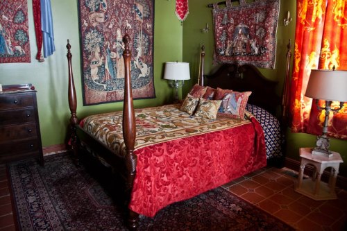 A cozy bedroom featuring a four-poster bed with colorful bedding, ornate tapestries, and warm-toned curtains.