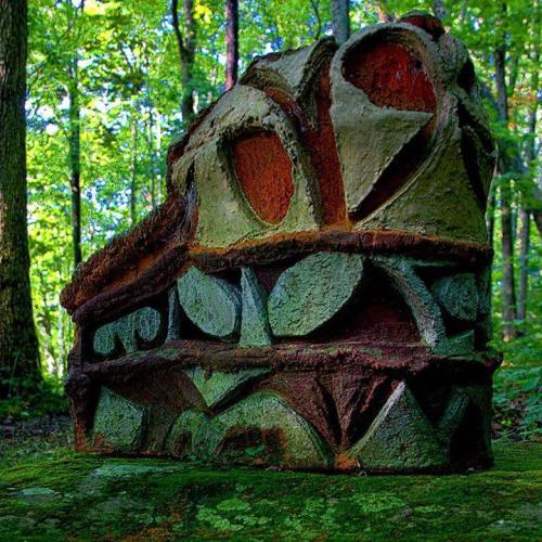 A colorful, abstract stone sculpture surrounded by lush green trees in a forest setting.