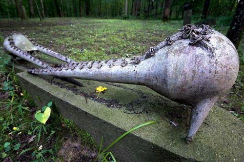 A large, abstract sculpture resembling an octopus, resting on a stone base in a wooded area.