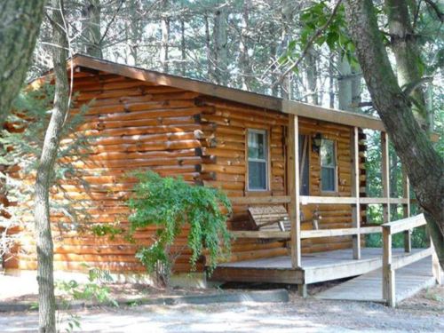 A cozy log cabin nestled among trees, featuring a wooden porch and surrounded by greenery.