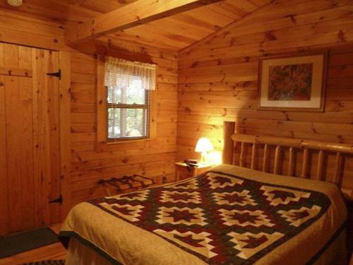 Cozy wooden bedroom with a quilted bedspread, a lamp, and a window, featuring rustic decor and warm lighting.