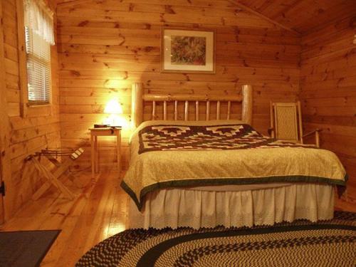 Cozy wooden bedroom with a quilted bed, a lamp, and rustic decor, featuring warm lighting and a woven rug.