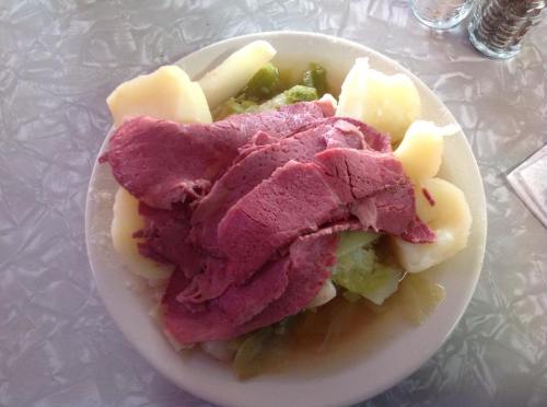 A plate of sliced corned beef served with boiled potatoes and greens in a light broth.