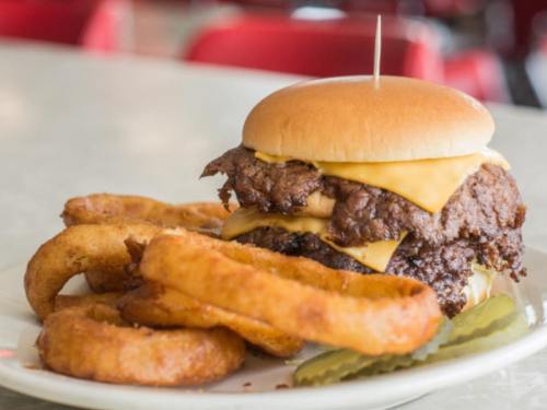 A juicy cheeseburger with crispy onion rings and pickles on a plate, set against a diner backdrop.
