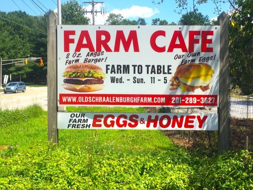 Sign for Farm Cafe promoting farm-to-table burgers and fresh eggs and honey, open Wednesday to Sunday, 11 AM to 5 PM.