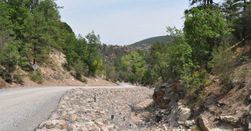 A winding gravel road surrounded by lush greenery and rocky terrain under a clear blue sky.