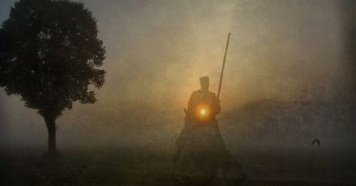 A silhouette of a horseman with a staff against a misty background, with a glowing sun behind them and a lone tree nearby.