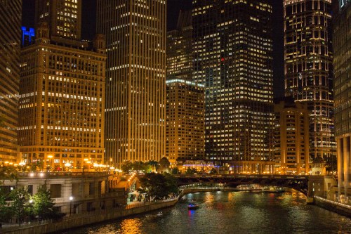 City skyline at night, featuring illuminated skyscrapers and a river reflecting the lights.