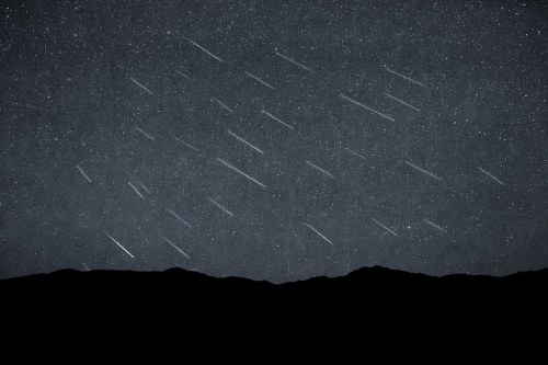 A starry night sky with streaks of light, resembling meteor trails, above a dark mountain silhouette.