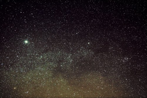 A starry night sky filled with countless stars and a faint greenish comet in the foreground.