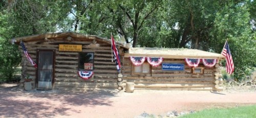 Log cabin building decorated with American flags and bunting, featuring a sign that says "Visitor Information."