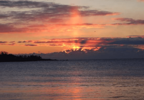 A vibrant sunset over calm waters, with colorful clouds and rays of light breaking through the horizon.
