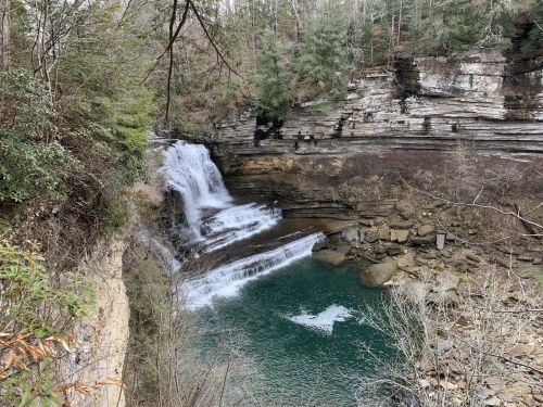 A serene waterfall cascades into a clear pool, surrounded by rocky cliffs and lush greenery.