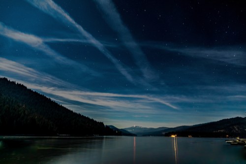 A serene night scene over a calm lake, with stars twinkling above and mountains silhouetted against the sky.