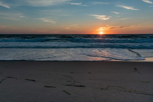 A serene beach at sunset, with gentle waves lapping at the shore and a colorful sky reflecting the fading light.