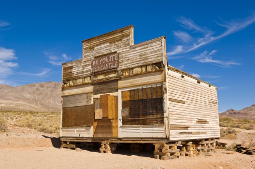 Abandoned wooden mercantile building in a desert landscape under a clear blue sky.