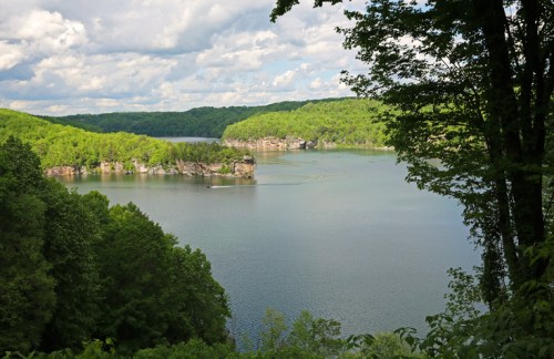 A serene lake surrounded by lush green hills under a partly cloudy sky.