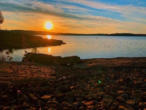 Sunset over a calm lake, with rocky shorelines and a colorful sky reflecting on the water's surface.
