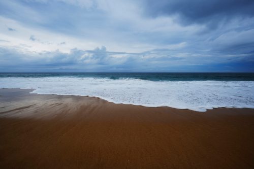 A serene beach scene with gentle waves lapping at the shore under a cloudy sky.