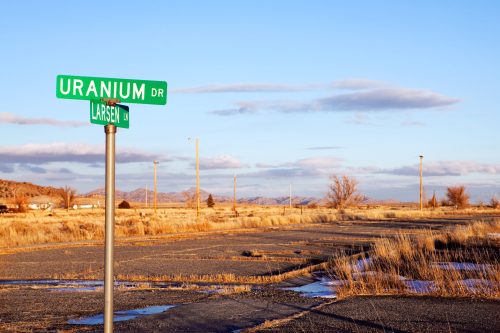 A street sign for Uranium Drive in a desolate landscape with a clear sky and distant mountains.