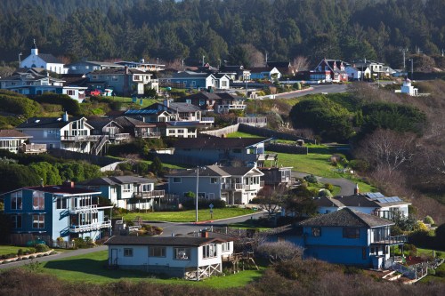 A scenic view of hillside homes surrounded by greenery and trees, with a clear blue sky in the background.