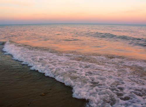 Gentle waves lapping at a sandy shore under a pastel sunset sky.