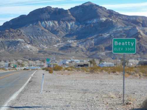 A road sign for Beatty, Nevada, with a mountain backdrop and speed limit signs along a desert highway.