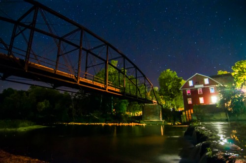 A night scene featuring a bridge over a river, with a red building and starry sky in the background.