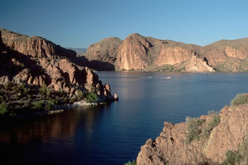 A serene lake surrounded by rugged mountains under a clear blue sky, with a small boat on the water.
