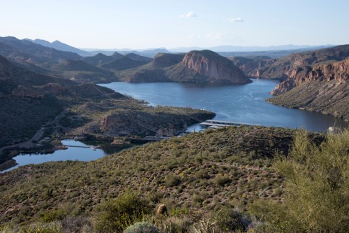A scenic view of a lake surrounded by mountains and desert vegetation under a clear blue sky.
