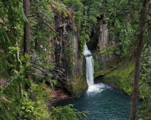 A serene waterfall cascades into a turquoise pool, surrounded by lush green trees and rocky cliffs.