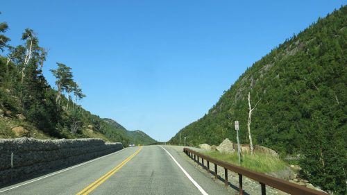 A scenic road flanked by steep green hills under a clear blue sky.