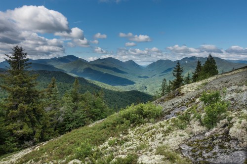 A panoramic view of lush green mountains under a blue sky with scattered clouds, showcasing a serene natural landscape.
