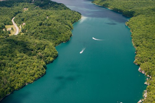 Aerial view of a serene lake surrounded by lush green forests, with boats gently gliding across the water.