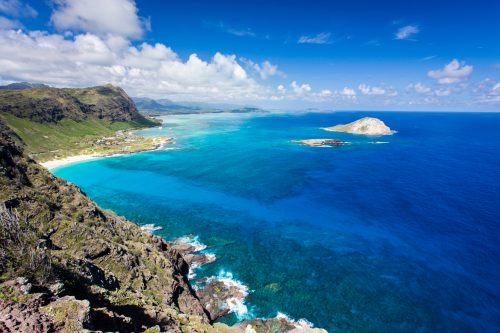 A stunning coastal view featuring turquoise waters, rocky cliffs, and a distant island under a bright blue sky.