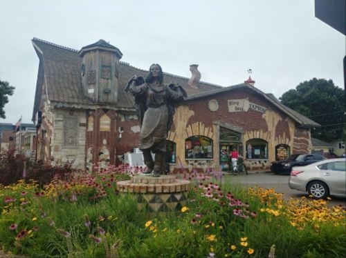 A whimsical brick building with a statue in front, surrounded by colorful flowers and visitors.