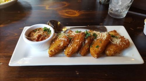 A plate of golden-brown fried snacks topped with cheese and herbs, served with a small bowl of dipping sauce.