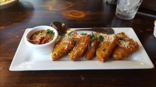 A plate of golden-brown fried snacks topped with cheese and herbs, served with a small bowl of dipping sauce.