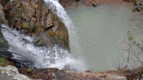 A waterfall cascading over rocks into a calm, shallow pool surrounded by greenery.