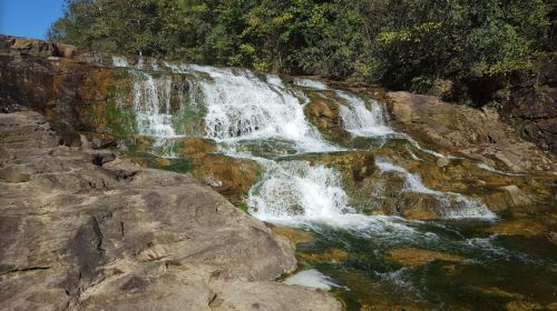A serene waterfall cascading over rocky terrain, surrounded by lush greenery and clear blue water.
