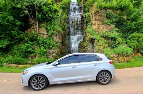A silver car parked beside a lush green landscape and a cascading waterfall.