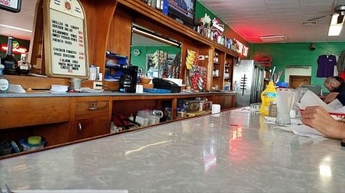 A diner counter with menus, condiments, and a customer in the background, featuring a casual, colorful atmosphere.