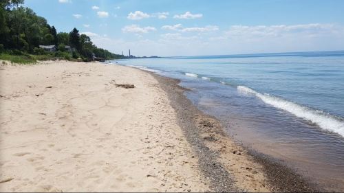 A serene beach scene with soft sand, gentle waves, and a clear blue sky in the background.
