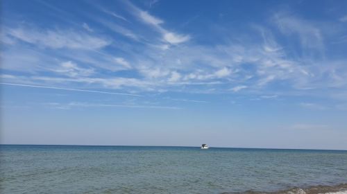 A serene seascape with calm blue waters, a clear sky, and a small boat in the distance.